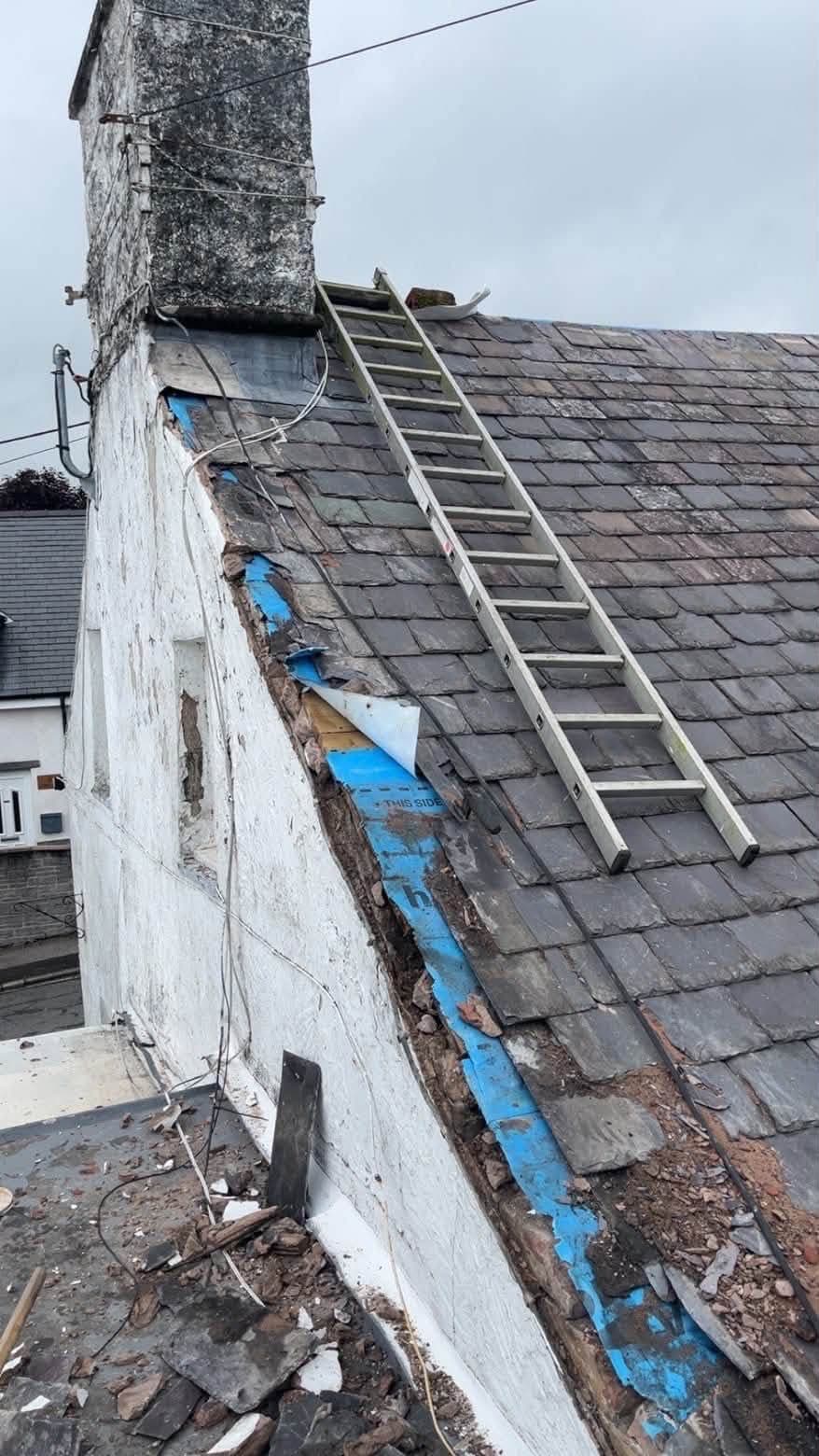 Damaged slate and torn felt along a gable end before the coping stones were reinstated
