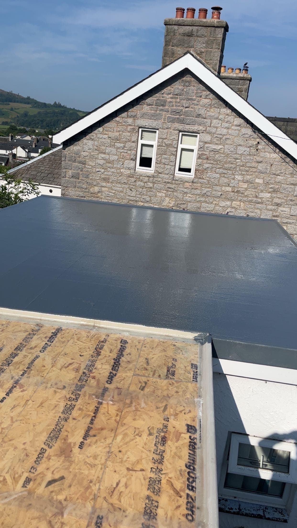 Completed grey GRP flat roof beside a stone gable and chimney
