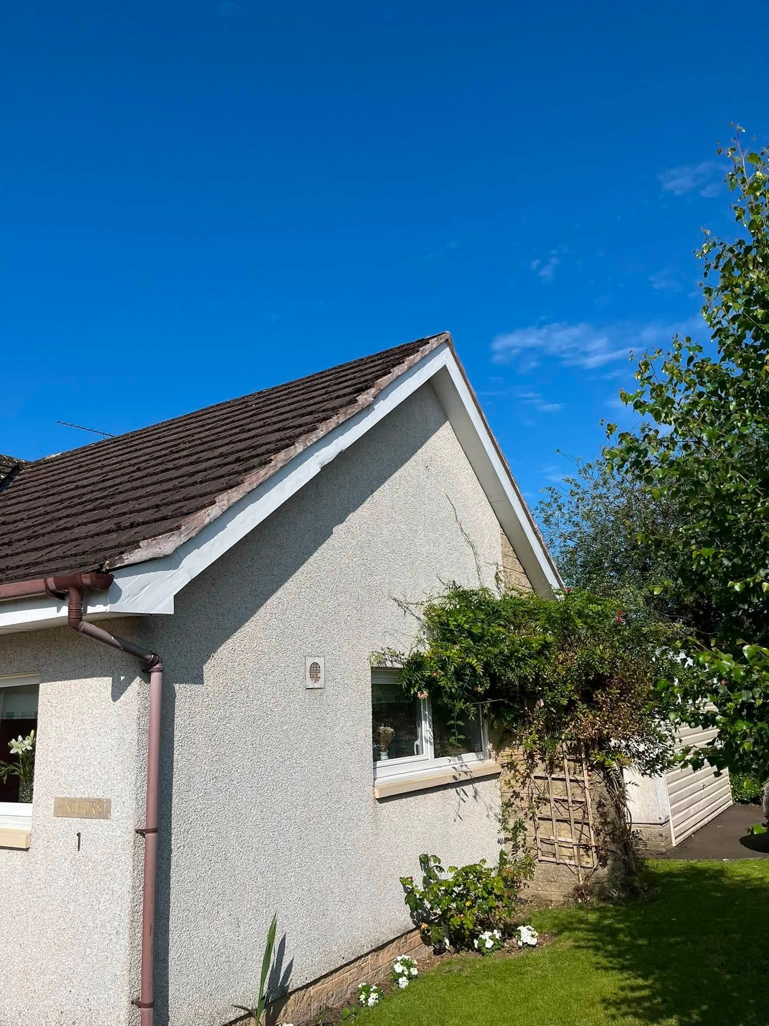 Existing bargeboard at a gable end before replacement, with worn felt at the ridge apex